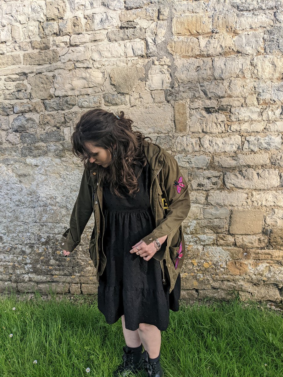 a messy haired shortarse wearing a lot of black and a patch-ridden khaki jacket
