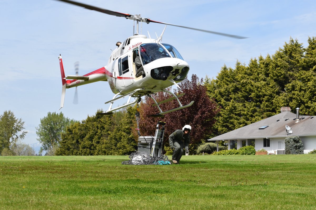 A helicopter hovers over an equipment load as a man moves out from under it.