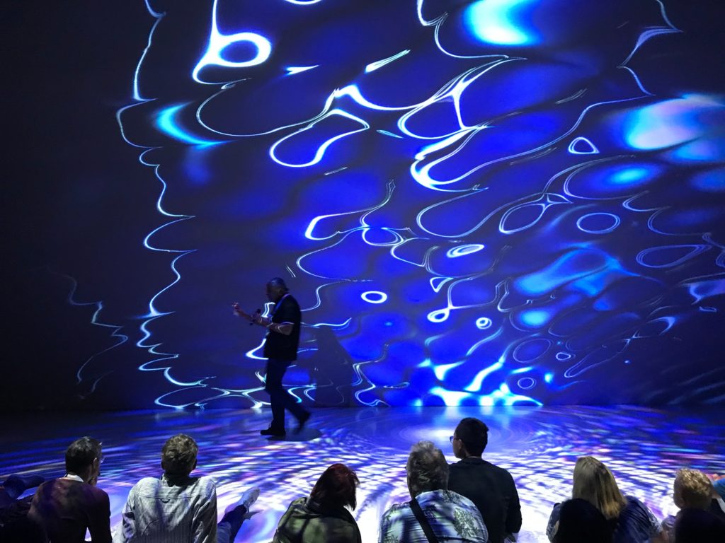 chav_ez's tweet photo. At the Ars Electronica Center Deep space 8k Theater 2019 screening of Quantum LOGOS (vision serpent) describing my artwork to the audience. Illustrated is a visual of the quantum field's rippling effects influencing everything around you. #aiartcommunity #aiart https://t.co/2YsPHqEwmW
