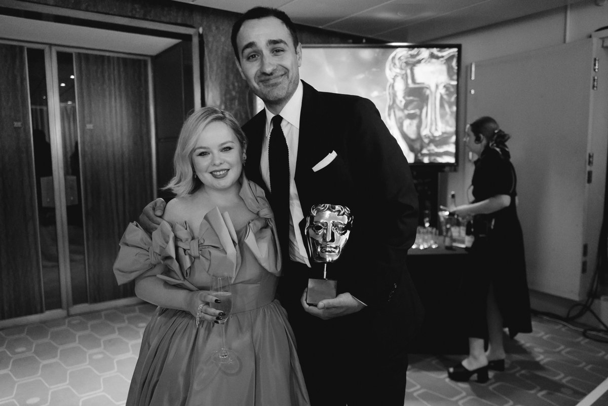 A set of black and white photos taken at the 2022 Virgin Media BAFTA TV Awards. 

Nicola Coughlan and Jamie Demetriou smile for the camera backstage. Jamie is holding his BAFTA. 
