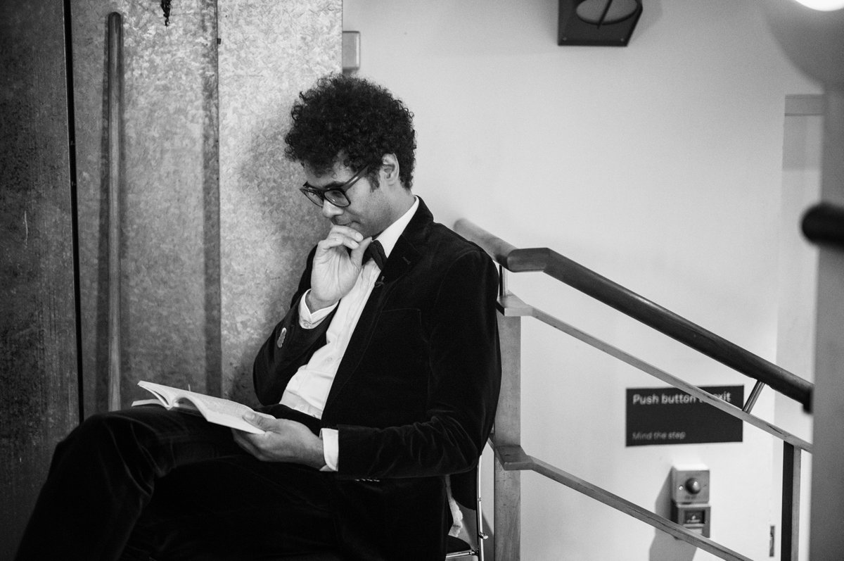 Richard Ayoade sits reading a book backstage