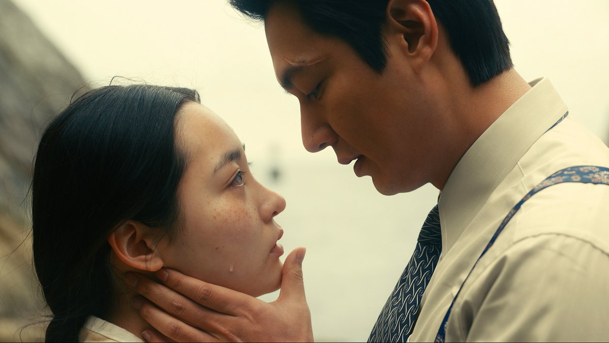 Minha Kim, as Sunja and Lee Min-ho, as Hansu, in Pachinko. Close-up shot of their profiles. He holds her chin in his hands and they are about to kiss.