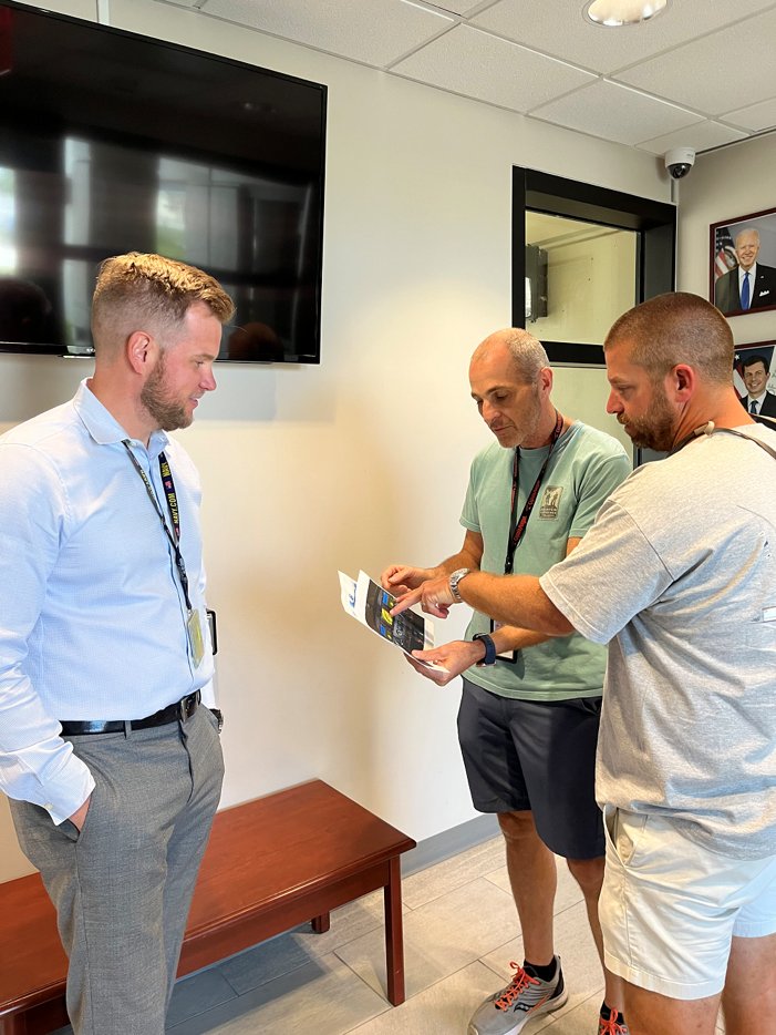 Image of Air Traffic Manager Ryan Warren (left) and Morgan (center) show the passenger printouts of the Cessna 208 flight deck they used to help him land safely at Palm Beach Airport. 