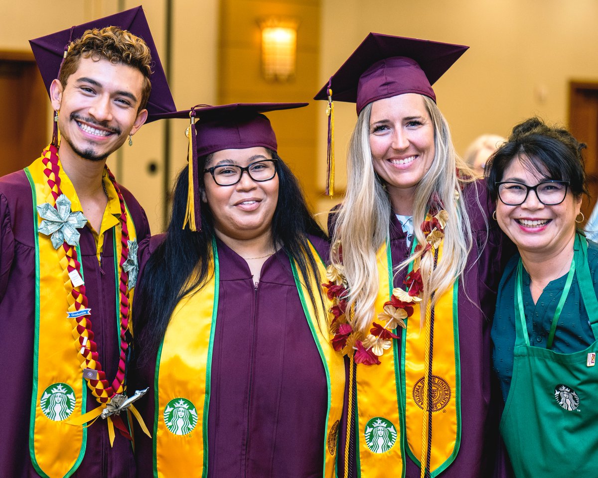 A group of four people of various ages and identities stand together smiling with their arms around each other. Three of them are wearing maroon Arizona State University graduation robes and caps with a yellow Starbucks stole and the fourth person is wearing a green Starbucks apron.