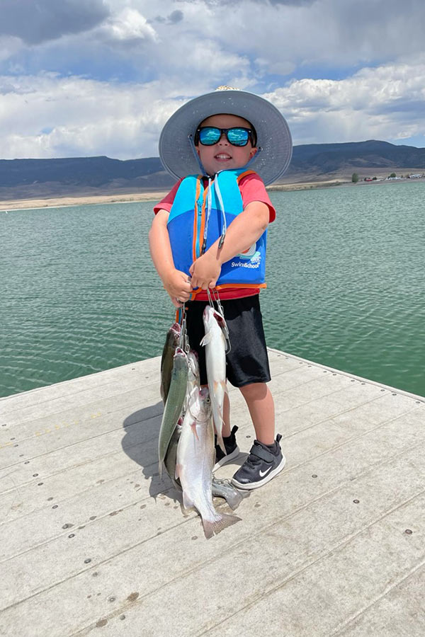 A child holding three large fish in front of a waterbody.