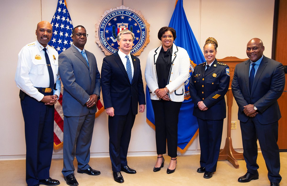 FBI Director Christopher Wray poses for a group photo with members of the Major Cities Chiefs Association on May 12, 2022, at FBI Headquarters. The American flag, the FBI flag, and the FBI seal are displayed behind them.
