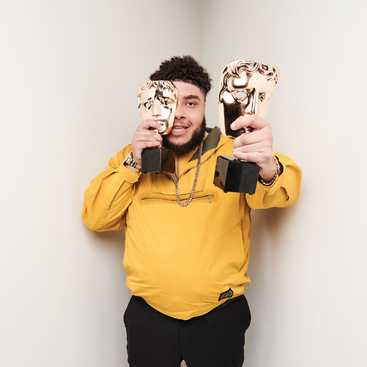 Big Zuu holds two BAFTAs, one near his face and one towards the camera