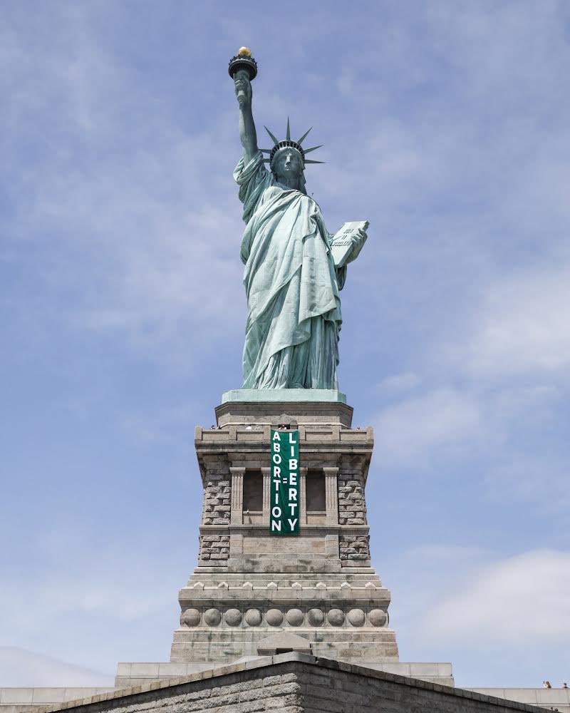 Image of the Statue of Liberty with a green banner draped from her feet that reads “Abortion = Liberty”