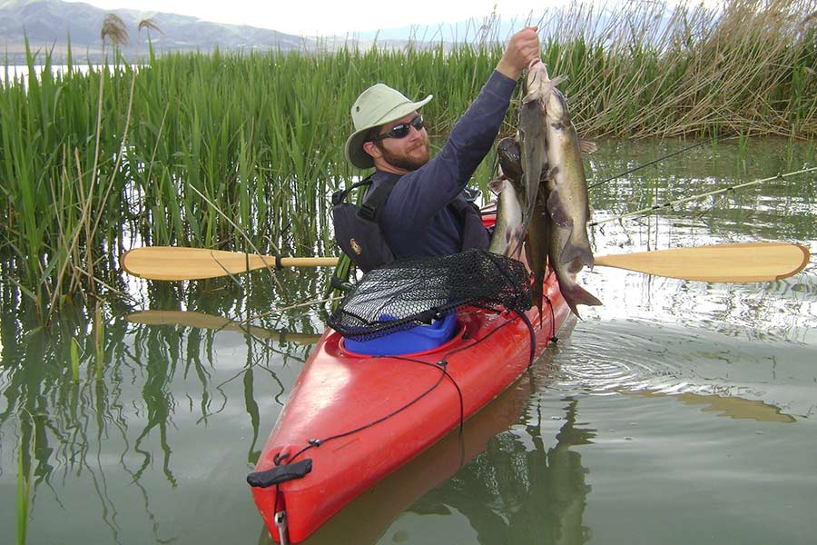 A man in a kayak in the water holding up a bunch of fish.