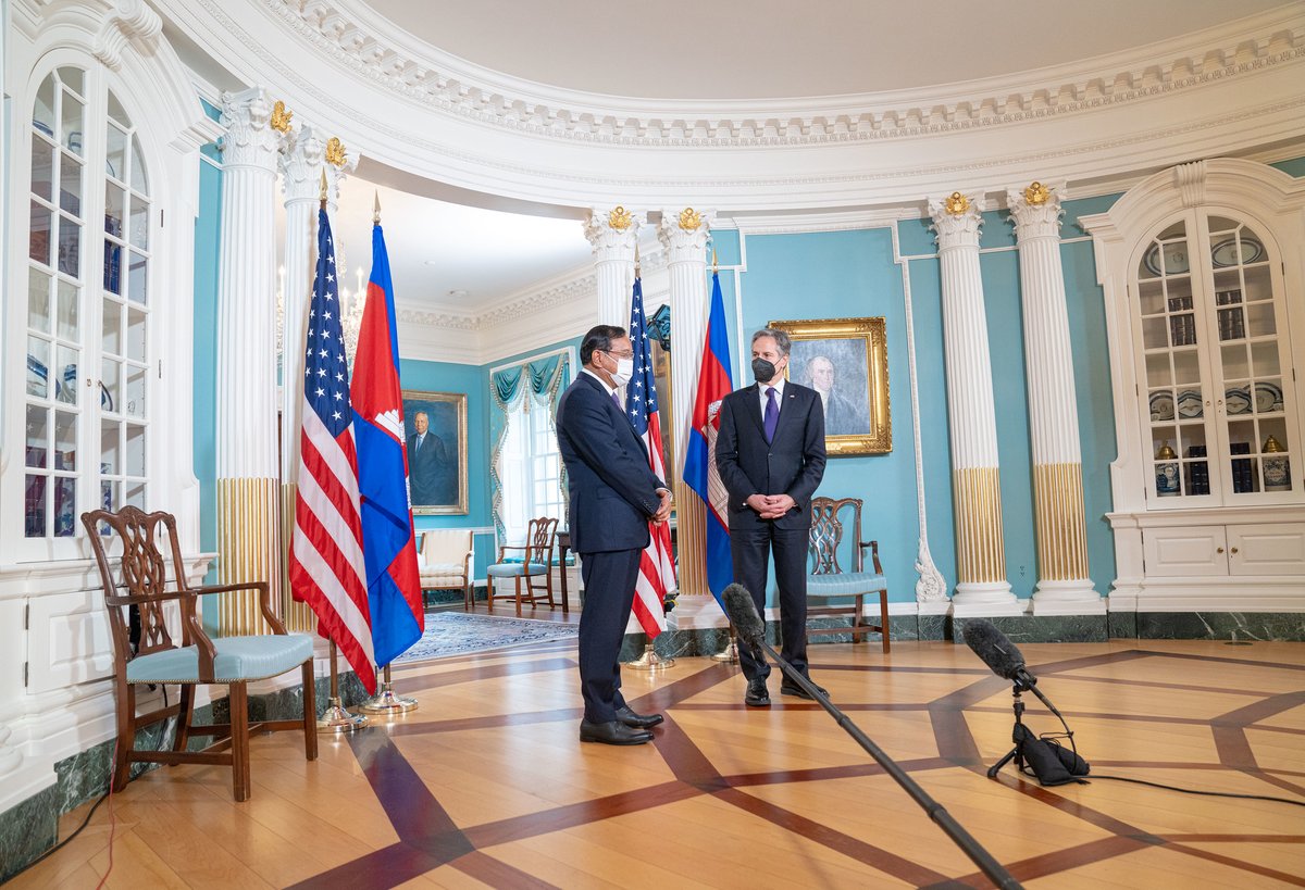 Deputy Prime Minister and Foreign Minister of Cambodia Prak Sokhonn and U.S. Secretary of State Antony Blinken stand safely distanced and masked in a round blue room at the State Department with their country's flags behind them.