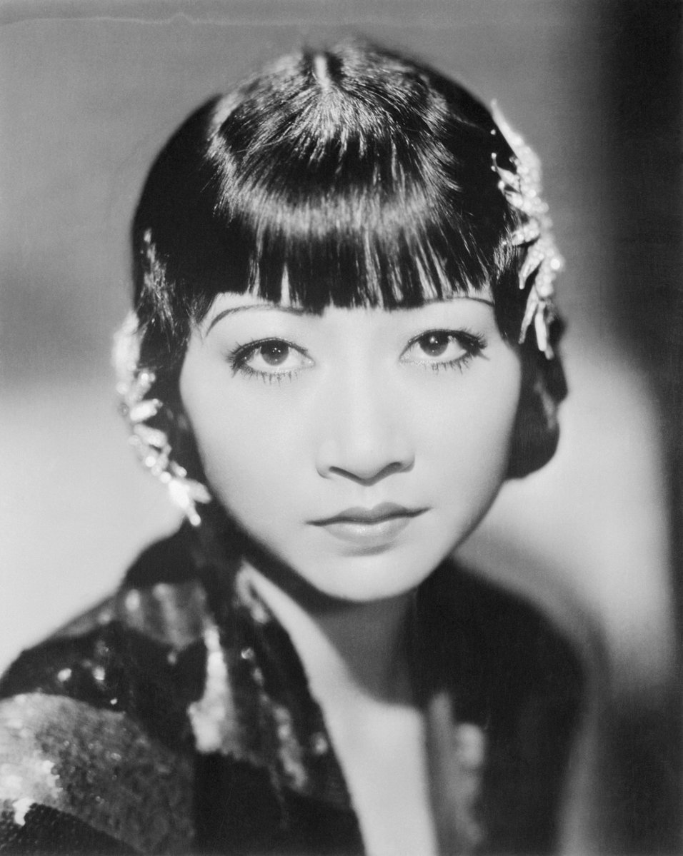 Actress Anna May Wong in medium close-up shot, wearing jewelled hair clasps and a patterned sequin gown