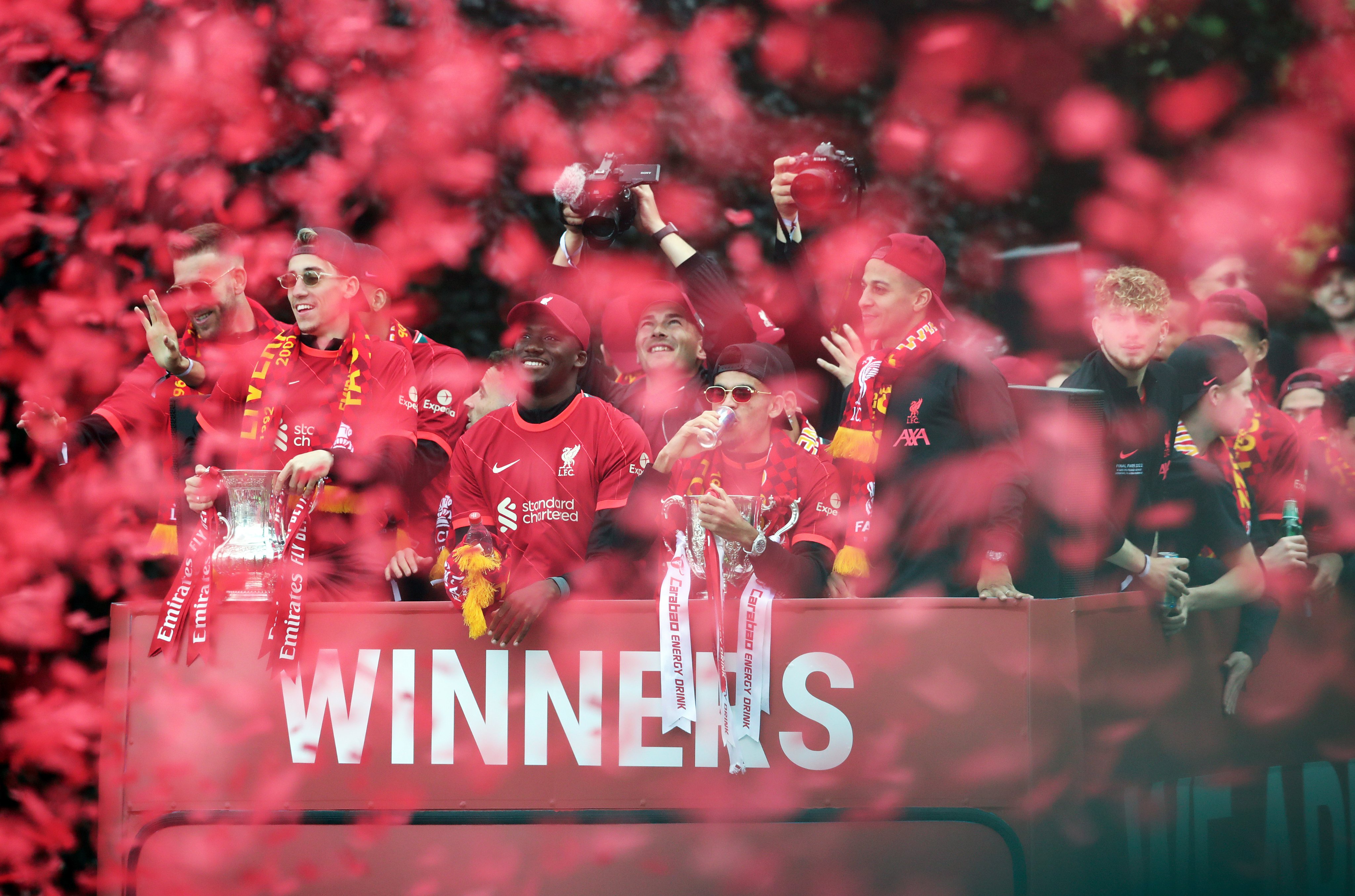 Kostas Tsimikas and Luis Diaz hold the FA Cup and the Carabao Cup Trophy with teammates during the trophy parade.