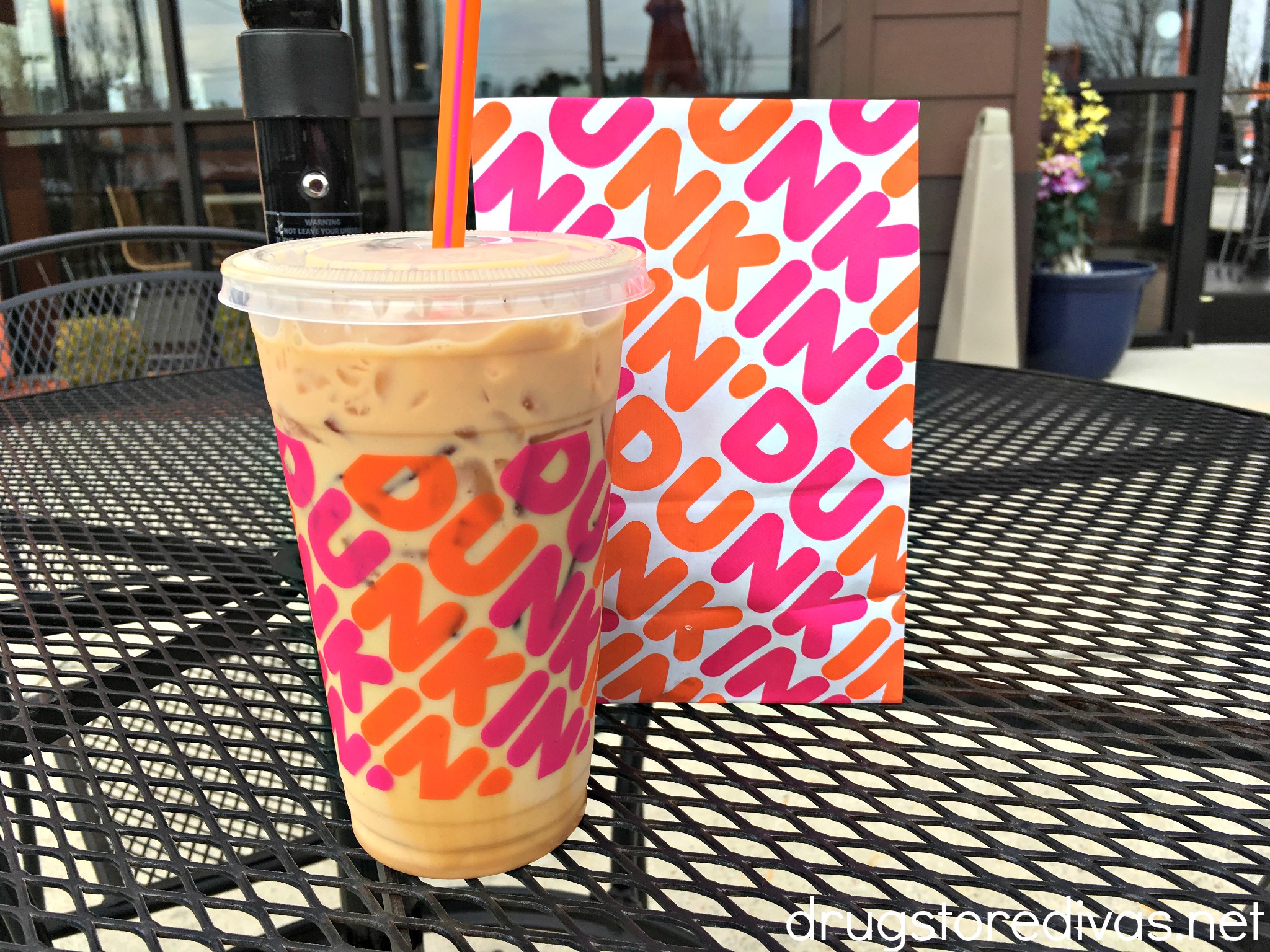 A Dunkin' drink and bag ion a table n front of a store.