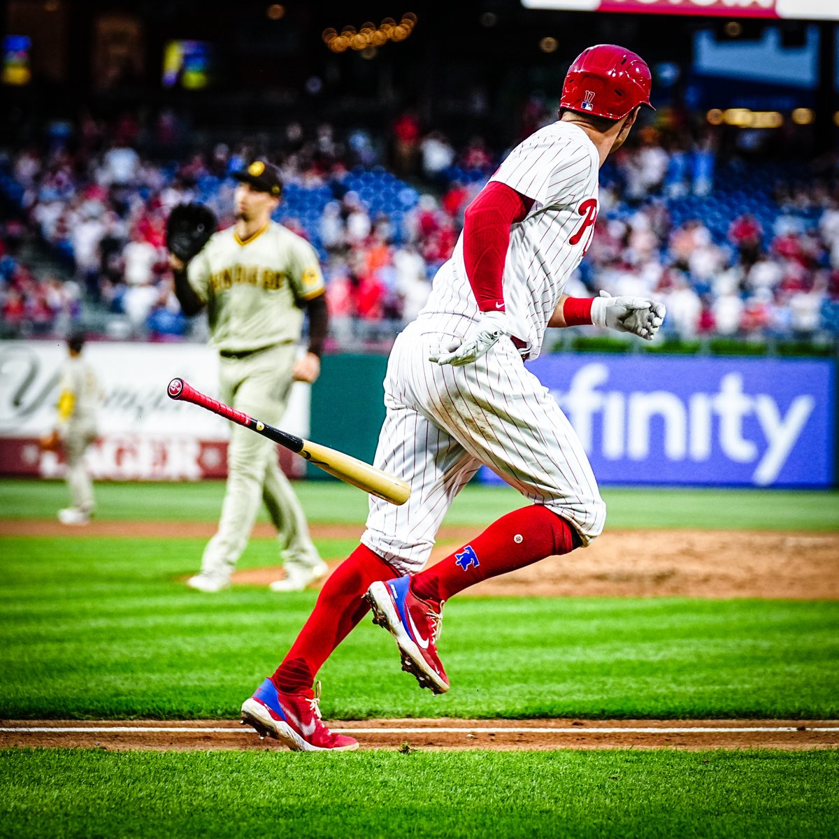 Rhys Hoskins in the red pinstripe uniform, watching the ball he just hit land in the stands for a home run.
