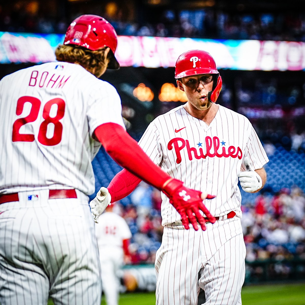 Rhys Hoskins and Alec Bohm, wearing the red pinstripe uniform, high five after Hoskins hits a home run.