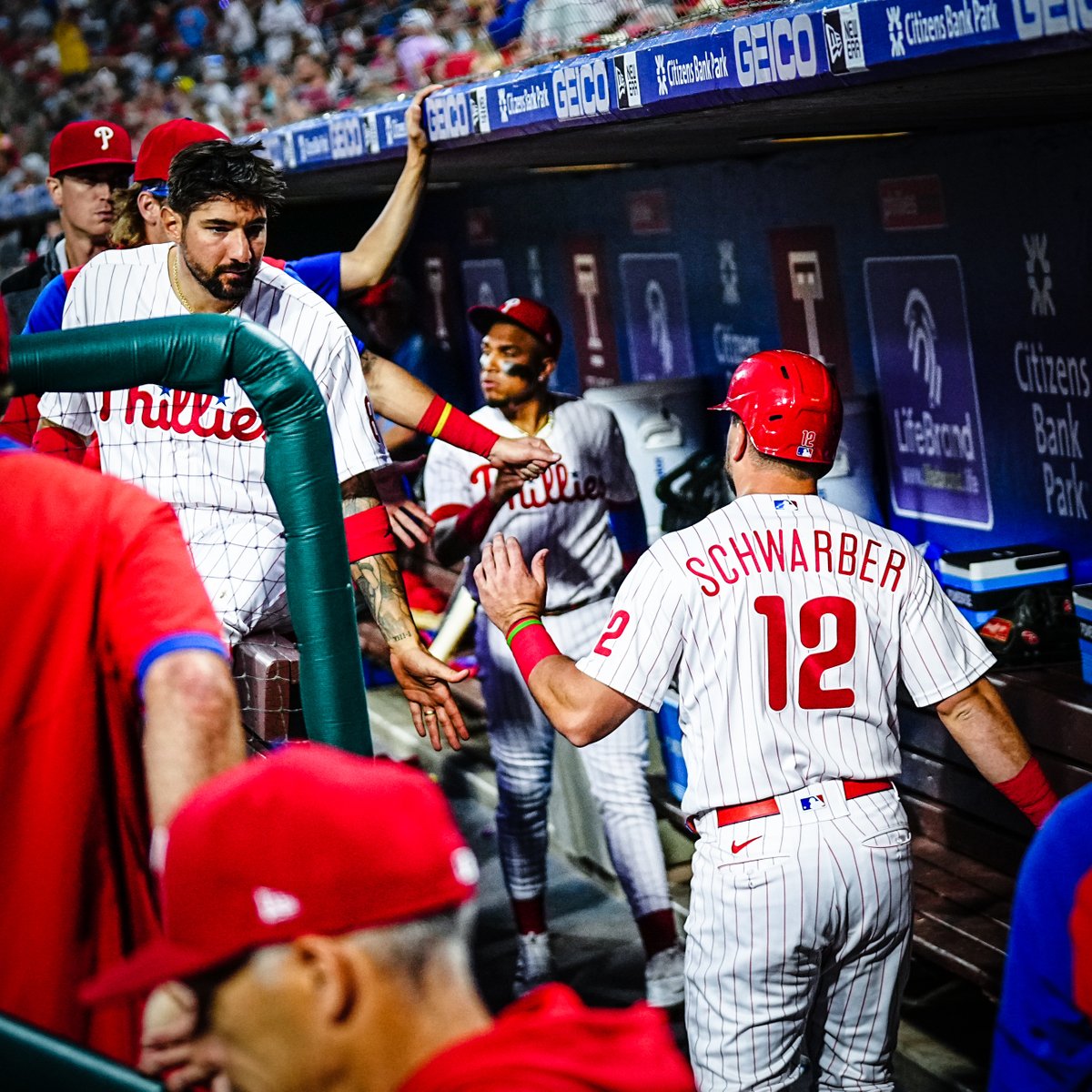 Kyle Schwarber, wearing the red pinstripe uniform, celebrating in the dugout after scoring a run.