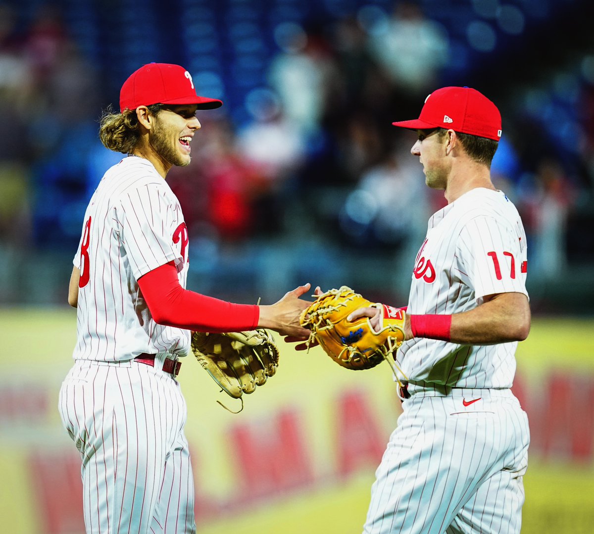 Alec Bohm and Rhys Hoskins, wearing the red pinstripe uniform, high-fiving after the Phillies win the game. Bohm is smiling.