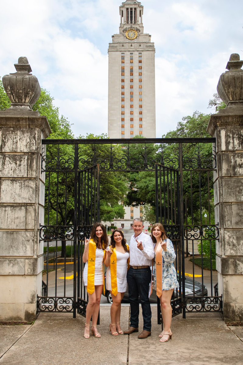 UT Austin President Jay Hartzell poses for a picture with three graduates with the Tower in the background.