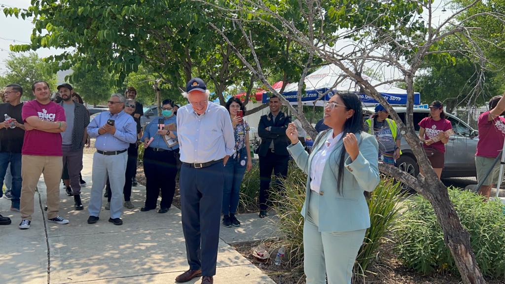 Bernie looking bashful, standing next to Jessica as she addresses a crowd outside