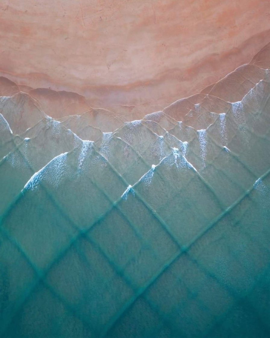 À Whangamata (Nouvelle-Zélande), deux systèmes de vagues se croisent à angles droits, dessinant une géométrie dynamique faite de carrés mobiles aux surfaces variables. Des collisions de surfeurs y sont structurellement possibles en l’absence de règles de priorité à droite.