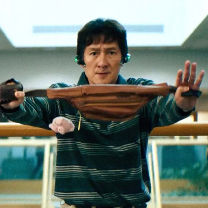 A film still of Ke Huy Quan in EVERYTHING EVERYWHERE ALL AT ONCE. He brandishes a fanny pack like a weapon, holding it out in front of him.
