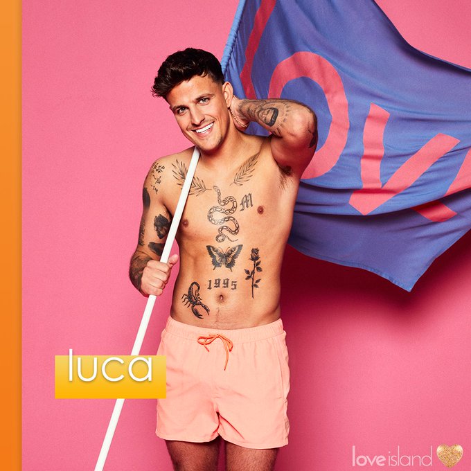 Man with tattoos on his torso wearing light orange swim shorts and holding a flag that says love