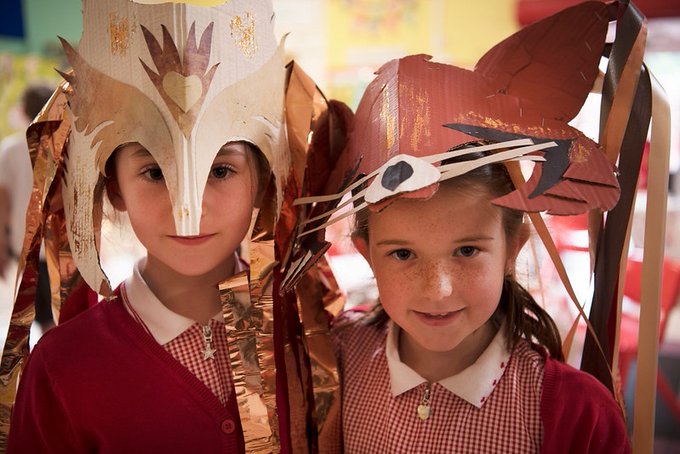 Two school children wearing cardboard animal masks, one is an owl the other is a fox