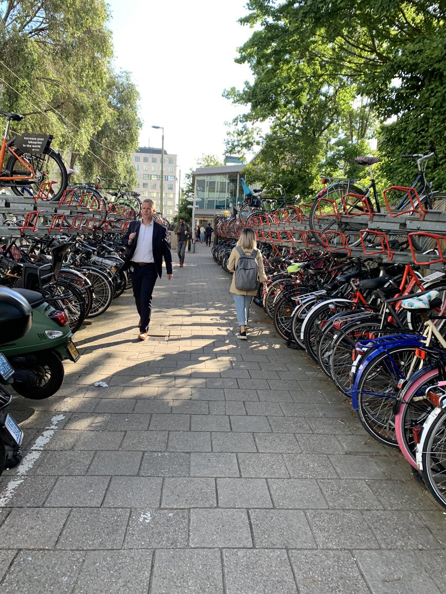 Looproute voetgangers naar Intercitystation Den Haag Laan v NOI. Je loopt tussen scooters en fietsenrekken, ontwijkt parkerende fietsers, en wandelt langs de hoge rand van een ongebruikte trambaan. #wandelstad #cid #stationsentree
