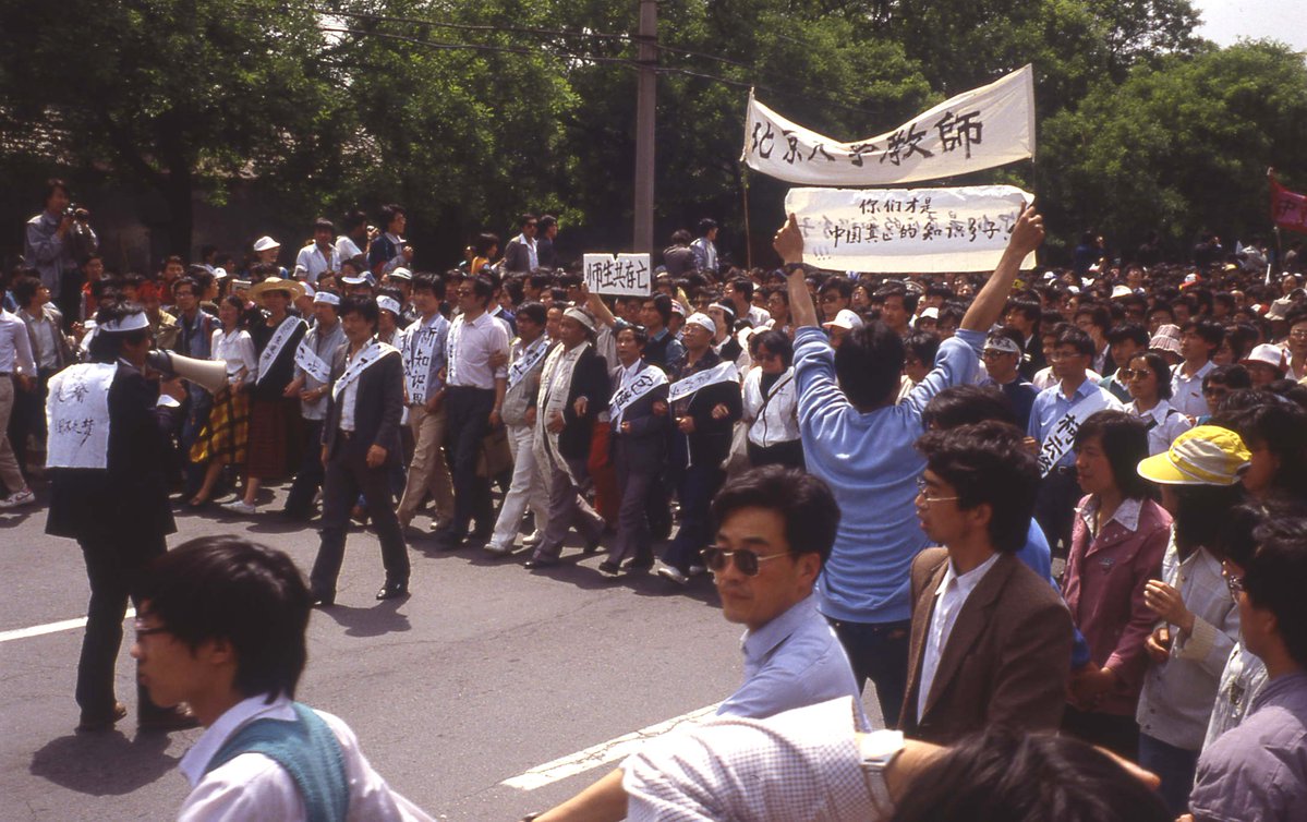 Beijing University professors marching to Tiananmen Square in 1989, in solidarity with student protesters. A professor holds a sign 'Teachers and students live and die together'. In foreground, a grateful student lifts a sign to them saying 'You are China's true intellectuals'.
