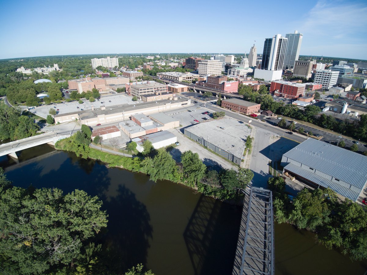 JohnMcGauley's tweet photo. Here's what six years of progress on the @RiverfrontFW ooks like. From a block of industrial buildings in 2016 (left) to @FortWayneParks Promenade Park in full bloom with the Riverfront at Promenade Park nearing completion (right). #FortWayne #Riverfront #redevelopment https://t.co/iiQ6jG51U8