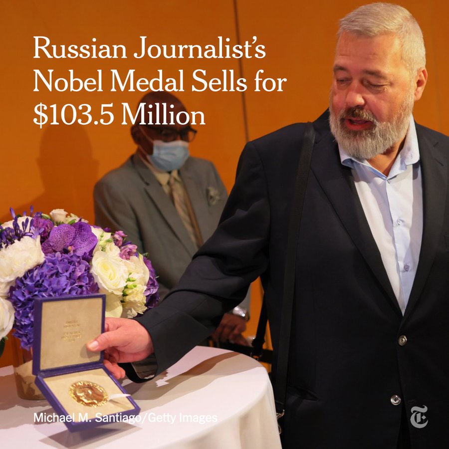 Dimitri Muratov holds his Nobel medal in his outstretched right hand. Muratov is speaking and looking at the medal, which is in an open box, and is standing in front of a table with a bouquet of white and purple flowers on it. Text reads: Russian journalist's Nobel medal sells for $103.5 million. Photo by Michael M. Santiago/Getty Images.