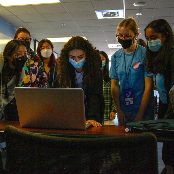 A group of women standing over a computer at VenusHacks.
