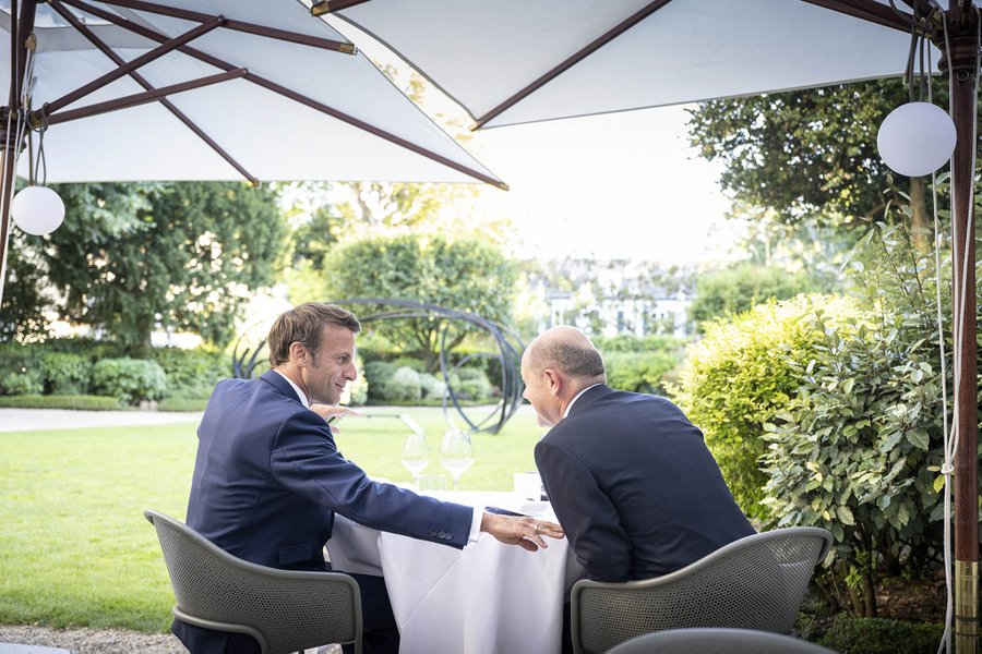 Foto: Präsident Macron und Bundeskanzler Scholz im Garten eines Restaurants in Paris im vertrauten Gespräch. Präsident Macron berührt Kanzler Scholz am Arm. 