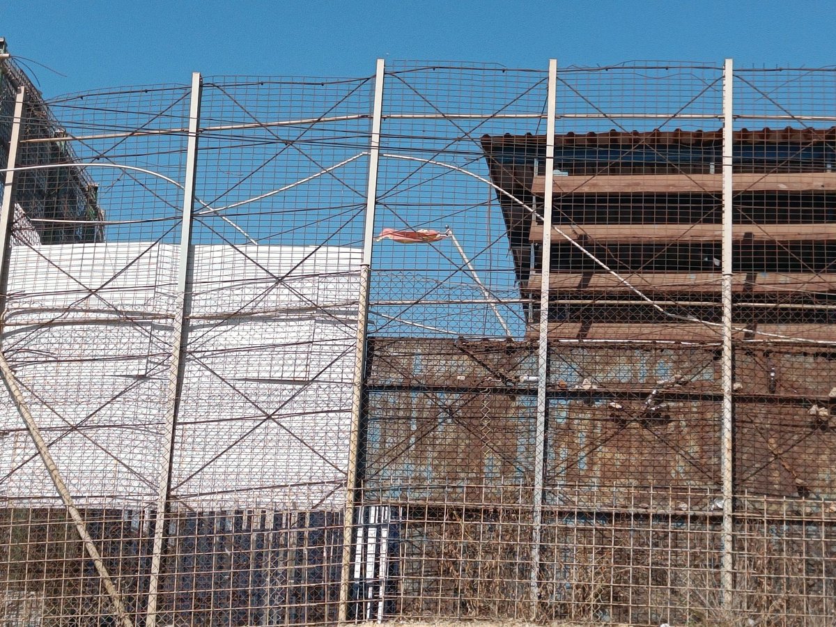 Gabriela_Schz's tweet photo. Los restos del último salto de la valla de Melilla, desde el lado español. Sobre esa garita (con la bandera española bien visible) se subieron agentes marroquíes para lanzar piedras a quienes estaban en lo alto de la alambrada. Los fallecidos y heridos, apilados al otro lado. https://t.co/yOkOwJVcuR