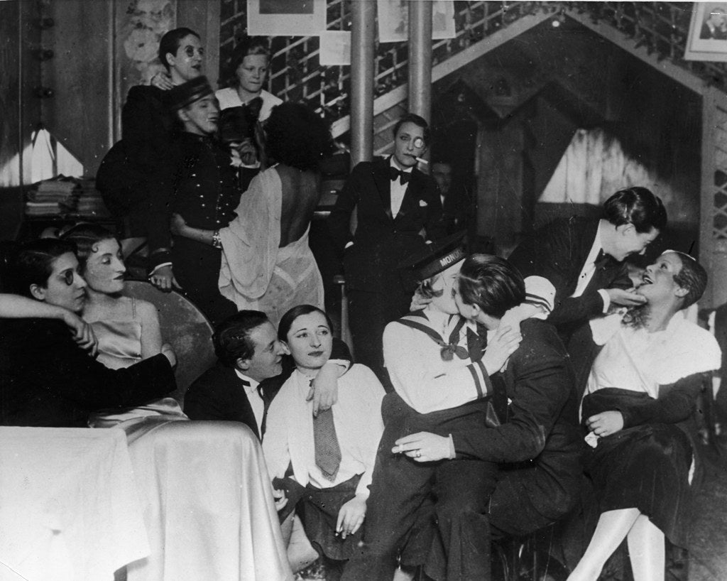 wikivictorian's tweet photo. 'A group of patrons, many dressed as men in tuxedos, and some with monocles, sit, talk, laugh, and kiss, at 'Le Monocle' a famous night club for women in Paris.' Photographed in the 1920s. https://t.co/j01ShBR52W