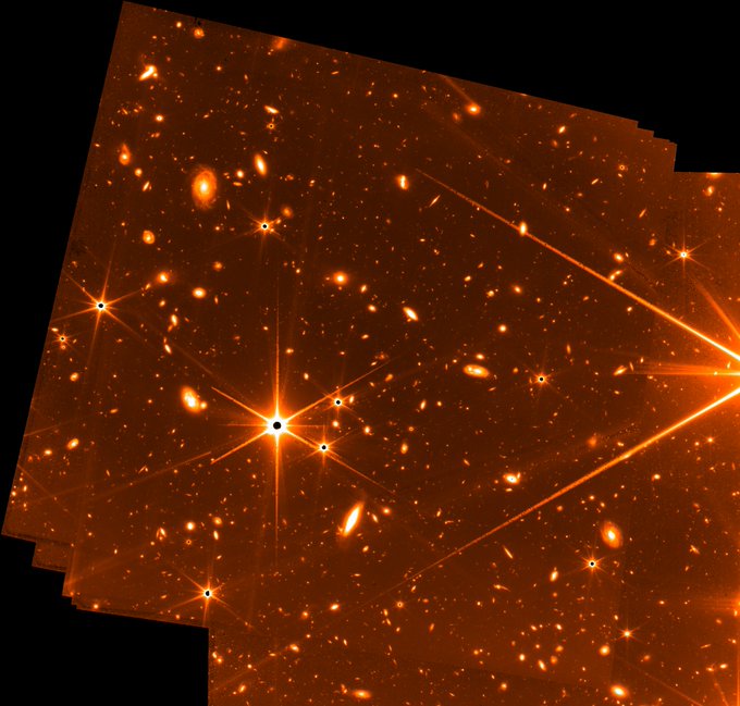 Bright stars (each with 6 spikes of light radiating from them) dominate the foreground, while the background is littered with galaxies. The image is reddish in tone, selected to optimize visual contrast. Mission managers have also been using this during Webb's commissioning to differentiate engineering images from the science images still to come.