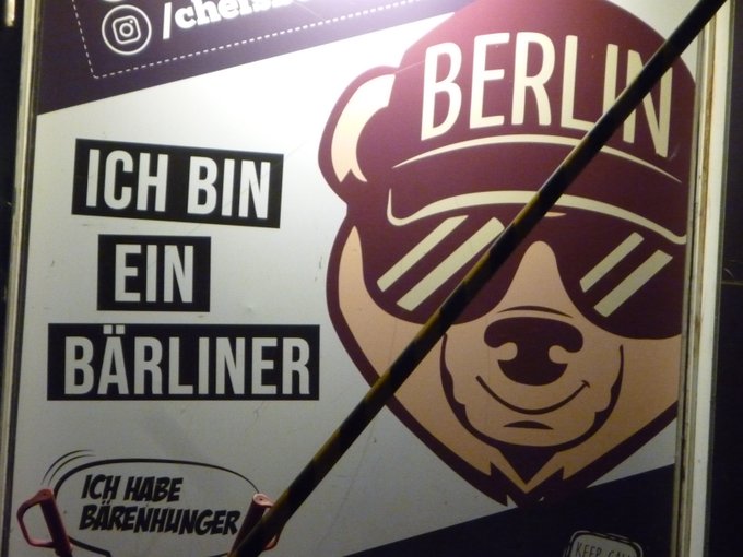 Ad panel showing a bear wearing sunglasses and a cap that reads "Berlin". Text by its side "Ich bin ein Bärliner" (play on words, "Bär" is "bear" and "Bärliner" sounds approximately like "Berliner") and "Ich habe Bärenhunger" ("I