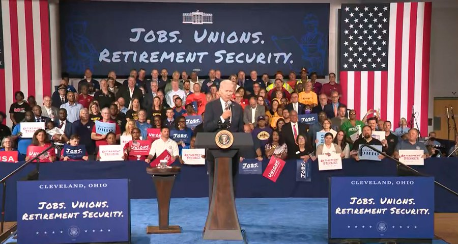 Image of President Joe Biden behind a podium. Behind him are supporters holding signs that say "JOBS" "UNIONS" "RETIREMENT SECURITY" 

Along with a backdrop behind them that says: JOBS. UNIONS. RETIREMENT SECURITY.

In front of him are two signs that read: CLEVELAND OHIO
JOBS. UNIONS. RETIREMENT SECURITY.