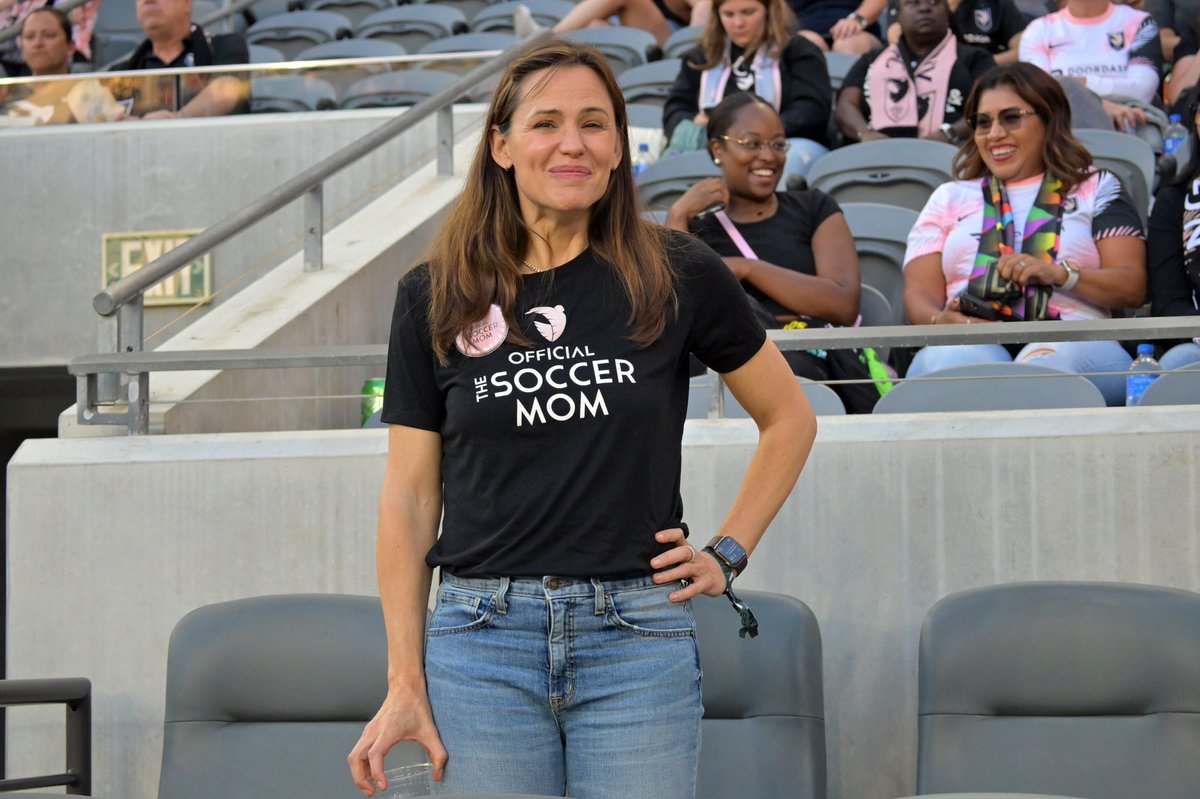 Jennifer Garner poses at the Angel City match in jeans and a ACFC branded t-shirt that says “official the soccer mom”