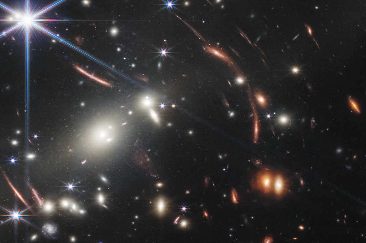AstroKatie's tweet image. Look closely at the "smudges" -- the stretched out swaths seen here as pink-ish streaks. Those are some of the most distant galaxies, with their light stretched and distorted by the gravity of the cluster of galaxies in the foreground, in what we call gravitational lensing. #JWST