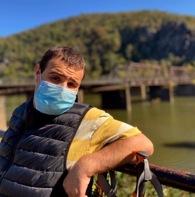 Cheers to smiles you can see through masks, beautiful summer days, and people who make you laugh. 🥰🌻

[Image description: Connor is shown in a yellow shirt with a black vest. He is wearing a mask. Behind him, a bridge over water is visible].