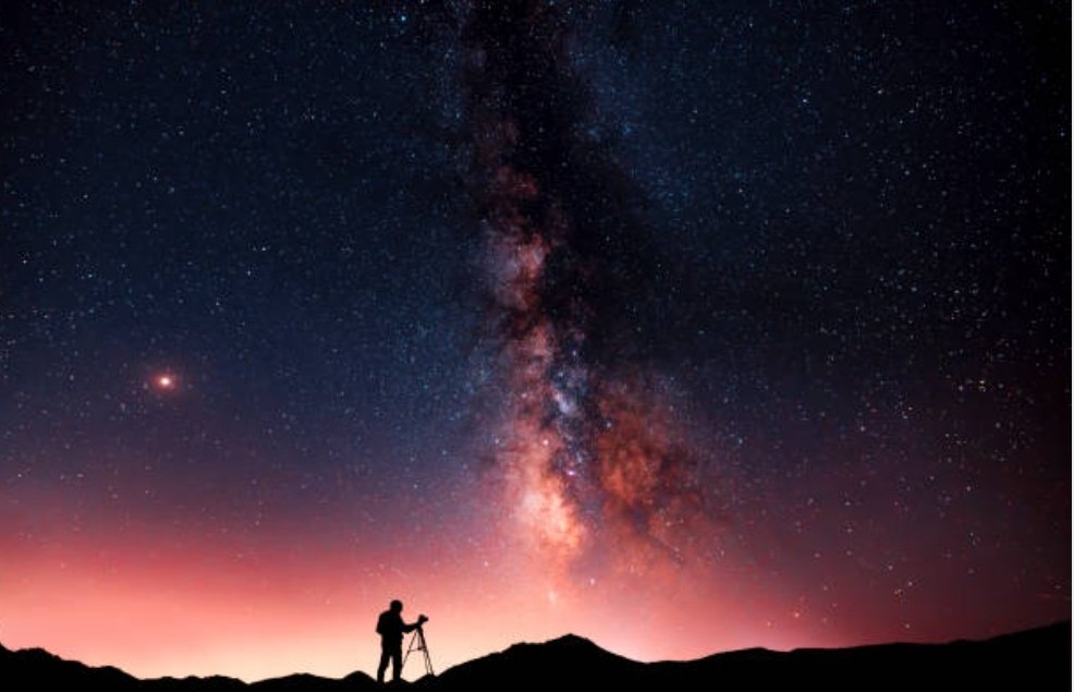 Beautiful starry night landscape. A silhouette of a photographer stands on a hill and looks at a beautiful starry sky