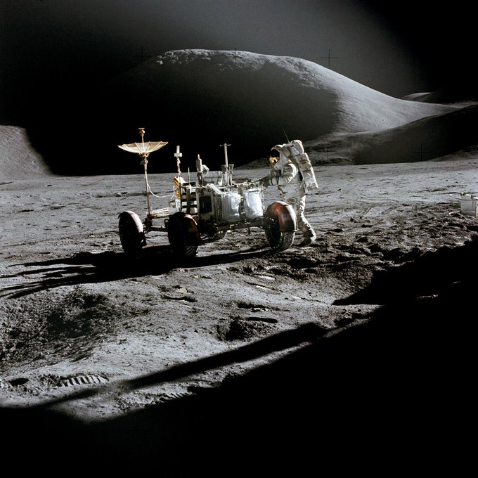 Astronaut James B. Irwin, lunar module pilot, works at the Lunar Roving Vehicle during the first Apollo 15 lunar surface extravehicular activity (EVA) at the Hadley-Apennine landing site. The shadow of the Lunar Module "Falcon" is in the foreground. This view is looking northeast, with Mount Hadley in the background. This photograph was taken by astronaut David R. Scott, commander.
