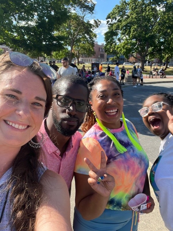 Four people smiling and giving a peace sign: Virginia Leigh on the left, and three community members from Lawrence next to her.