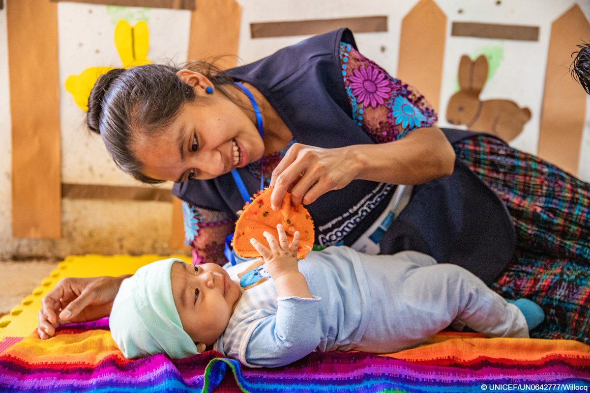  A mother is smiling while holding an orange cloth toy and playing with her baby.