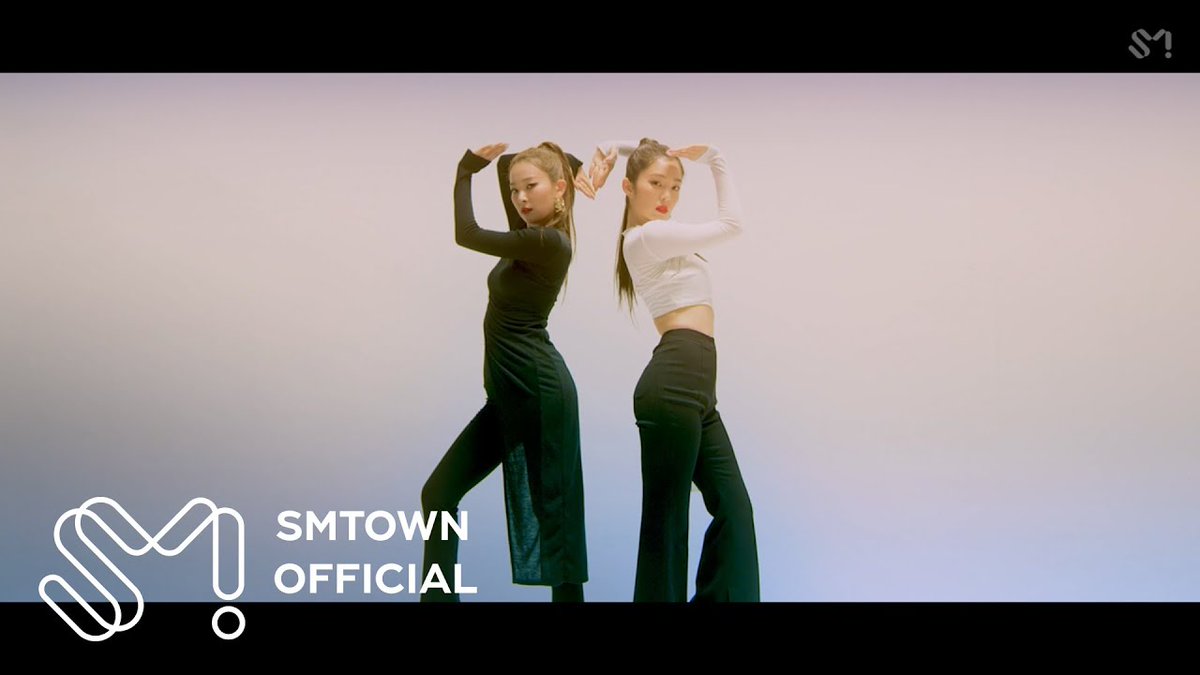 Two female performers dance in matching black outfits against a pale background, with 'SMTOWN OFFICIAL' branding visible in the lower left corner.