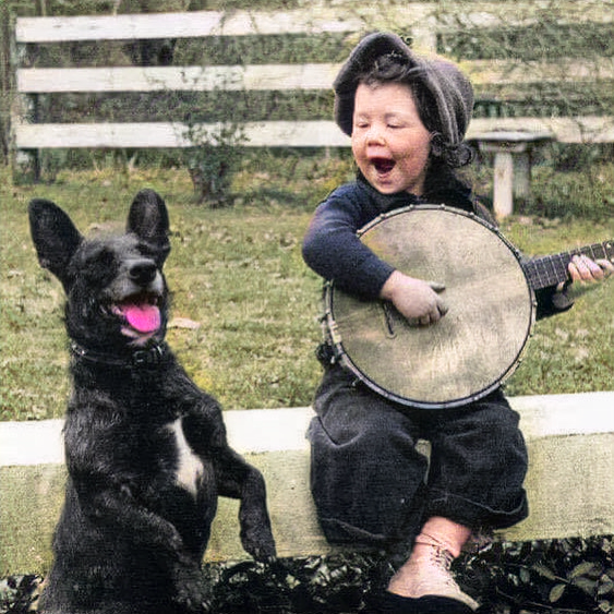 A young boy playing the banjo with his dog, 1920.