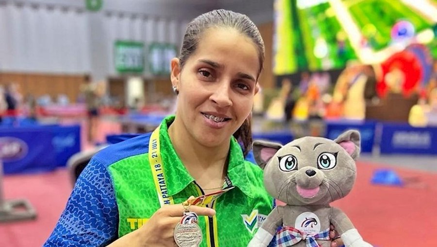 Foto da atleta Catia Oliveira, do tênis de mesa, segurando sua medalha de prata e o mascote da competição.