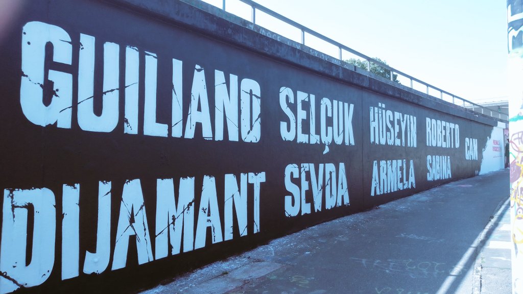 Eine schwarz gesprühte Betonwand, darauf die Namen der Opfer des rassistischen Anschlags am OEZ in München vom 22. Juli 2016:<br><br>Guiliano  Selçuk  Hüseyin  Roberto  Can<br>Dijamant  Sevda  Armela  Sabina