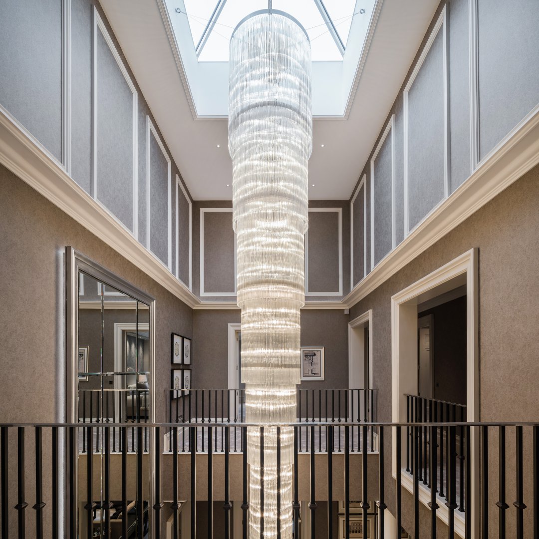 This bespoke chandelier mirrors the curvature of this magnificent stone staircase as it cascades 8m down 2 flights of stairs - beautifully framed by the concealed lighting in the steps and enhanced by the tactile suede wallpaper in warm taupe.